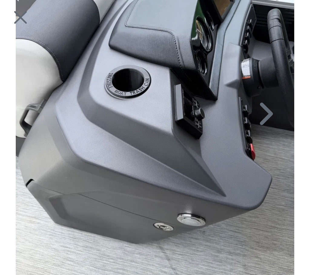 A close-up of a gray vehicle interior trim panel with a circular cup holder, control buttons, and part of the steering wheel visible.